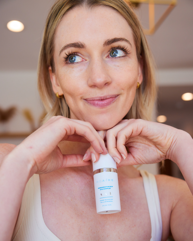 Smiling woman holding Regenerative ECM Eye Complex bottle in gallery position 1 with soft natural lighting and warm background