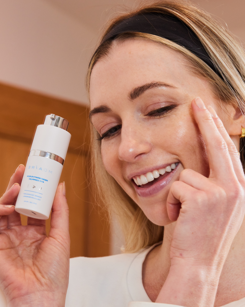 Happy woman gently touching eye area while holding Regenerative ECM Eye Complex in gallery position 1