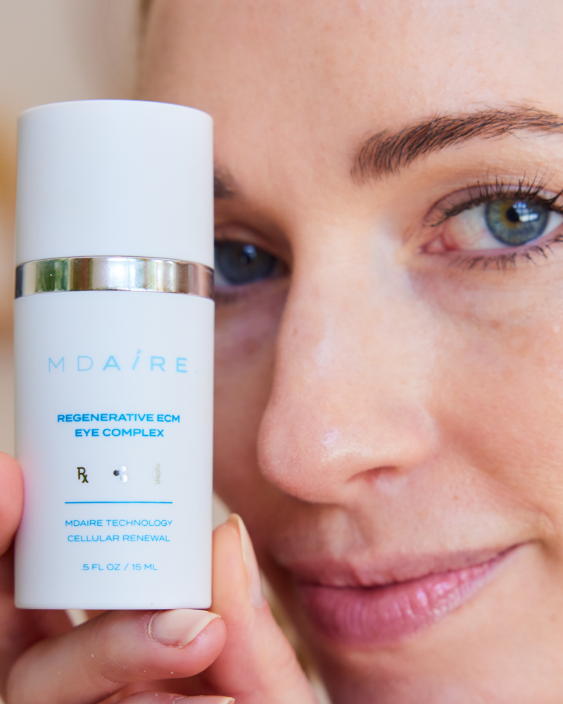 Close-up of woman holding Regenerative ECM Eye Complex bottle in gallery position 1 with clear focus on product label and face
