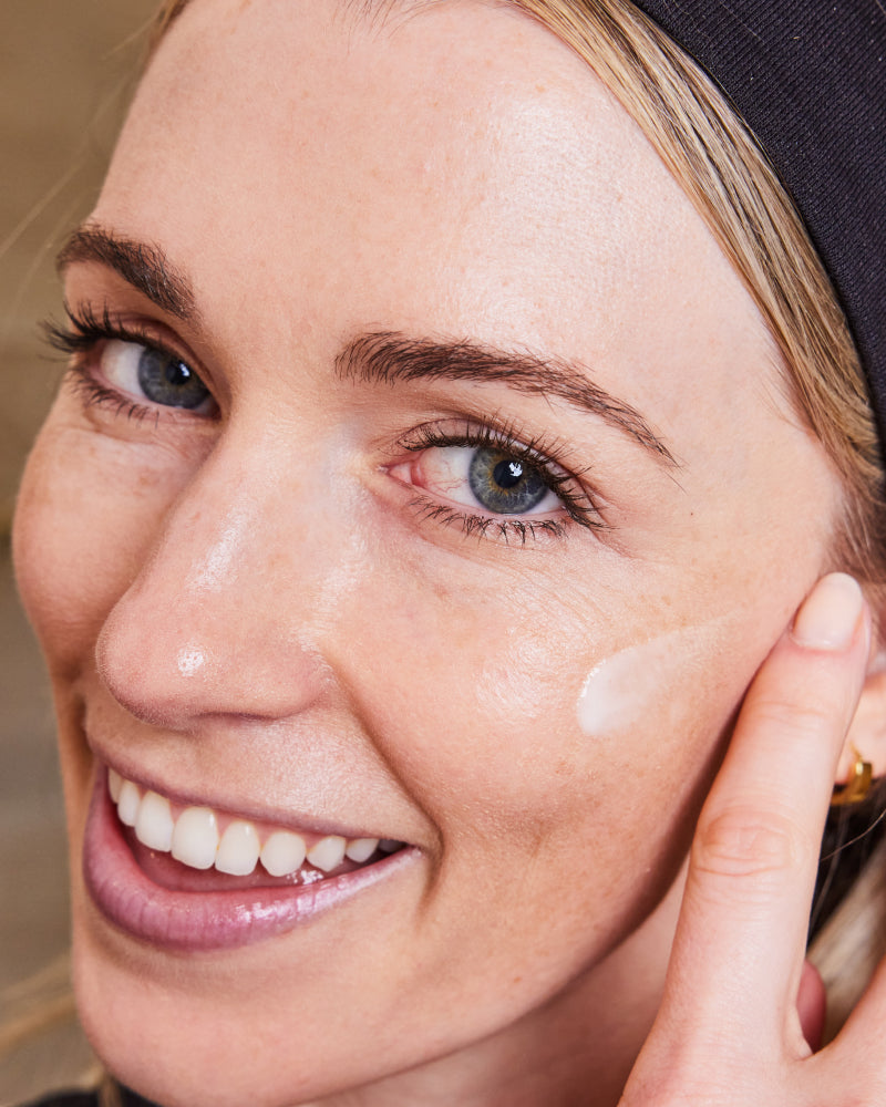 Smiling woman applying Everyday Hydration Duo cream to cheek showcasing skin hydration and glow gallery position 1
