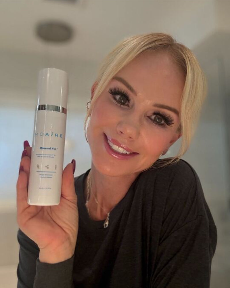 Woman smiling while holding a bottle of Mineral Fix³ Sunscreen with silver accents gallery position 1