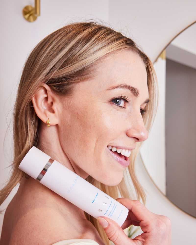 Smiling woman holding Neck Tyte-R moisturizer close to her neck with white bottle and silver band gallery position 1
