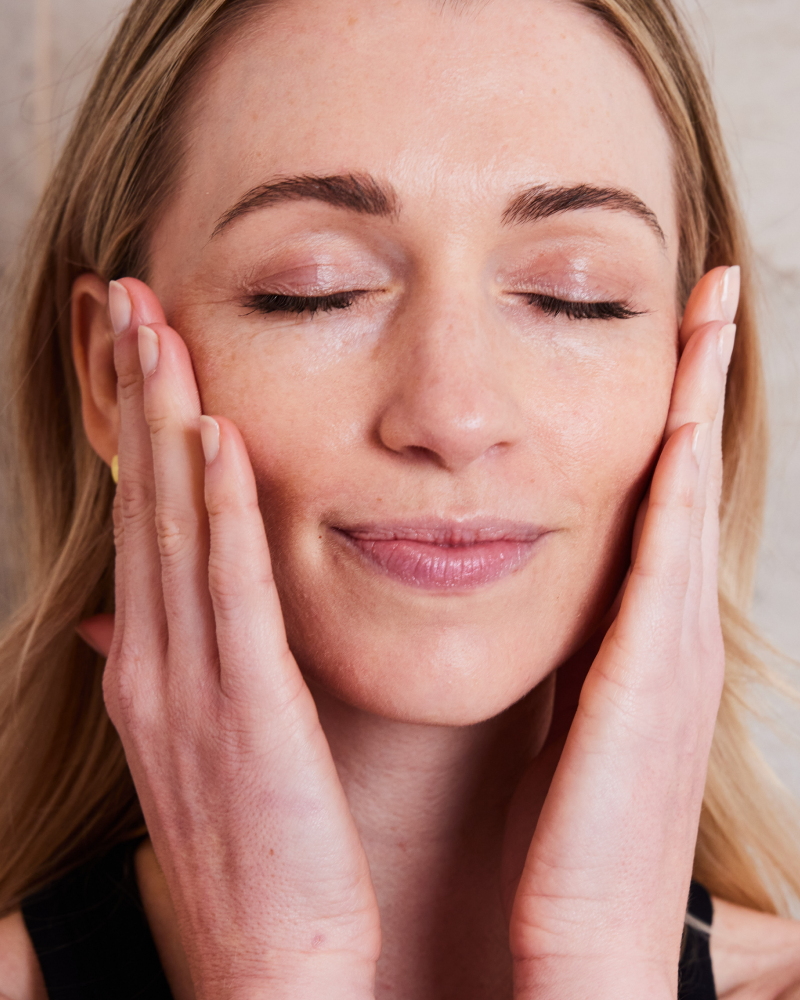 Woman gently touching her face with glowing skin, embracing Healthy Skin From Within using RXR Retinol Anti-Aging Serum developed by Dr. Stefani Kappel