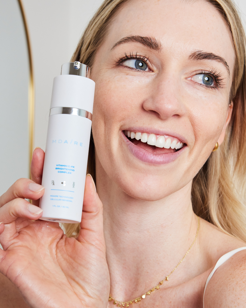 Smiling woman holding Vitamin C-FK  Brightening Complex bottle close to face in gallery position 1