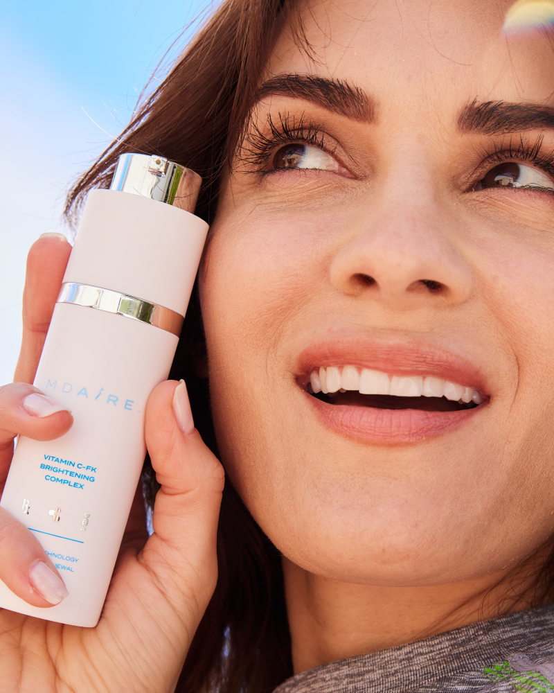 Woman smiling and holding Vitamin C-FK  Brightening Complex bottle close to face in gallery position 1