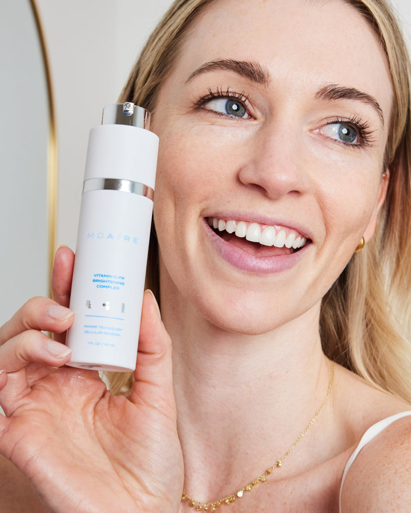 Woman smiling while holding Correct and Protect Duo in gallery position 1 with bright, clear skin and gold hoop earring