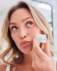 Rush Hour Duo with woman holding open jar of eye cream near cheek in gallery position 1 close-up shot